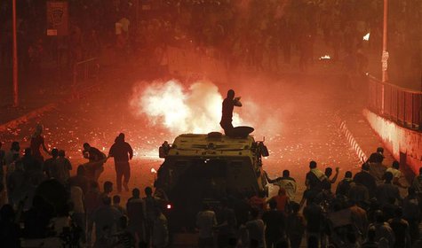 A riot police officer, on a armoured personnel carrier surrounded by anti-Mursi protesters (foreground), fires rubber bullets at members of A riot police officer, on a armoured personnel carrier surrounded by anti-Mursi protesters (foreground), fires rubber bullets at members of