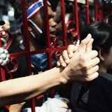 An anti-government protester touches the hand of a police officer through the main gate of the Thai Police Headquarters in Bangkok December An anti-government protester touches the hand of a police officer through the main gate of the Thai Police Headquarters in Bangkok December