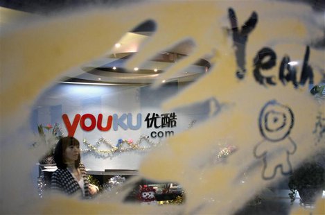 An employee is seen through a glass wall as she walks past the logo of Youku.com above the reception desk at the company's headquarters in B An employee is seen through a glass wall as she walks past the logo of Youku.com above the reception desk at the company's headquarters in B