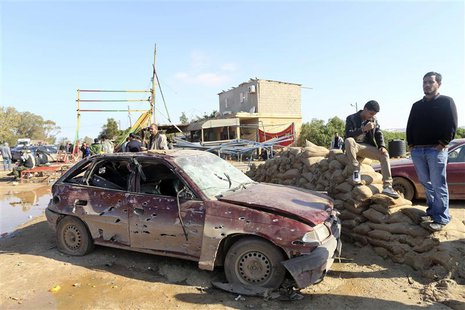 Men look at the scene near a military base in Barsis, some 50 km (30 miles) outside Benghazi, after a suicide bomber detonated a truck packe Men look at the scene near a military base in Barsis, some 50 km (30 miles) outside Benghazi, after a suicide bomber detonated a truck packe