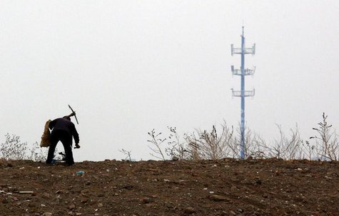 A mobile phone tower is seen behind a man carrying a pick over his shoulder as he walks past an area that will soon be a construction site o A mobile phone tower is seen behind a man carrying a pick over his shoulder as he walks past an area that will soon be a construction site o
