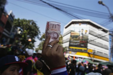 An anti-government protester holds up a Thai banknote to donate to anti-government protest leader Suthep Thaugsuban during a rally in centra An anti-government protester holds up a Thai banknote to donate to anti-government protest leader Suthep Thaugsuban during a rally in centra