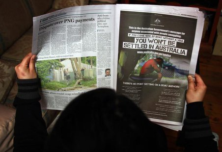 A woman reads a newspaper containing an advertisement (R) publicising the Australian government's new policy on asylum seekers arriving by b A woman reads a newspaper containing an advertisement (R) publicising the Australian government's new policy on asylum seekers arriving by b