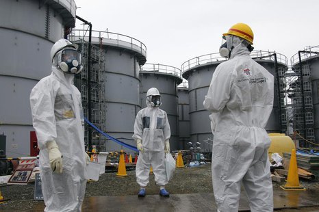 Tokyo Electric Power Corp's (TEPCO) official (C) and journalists wearing protective suits and masks stand in front of storage tanks for radi Tokyo Electric Power Corp's (TEPCO) official (C) and journalists wearing protective suits and masks stand in front of storage tanks for radi