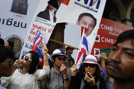 Under a damaged pre-election poster of Thai Prime Minister Yingluck Shinawatra, anti-government protesters blow whistles as they greet fello Under a damaged pre-election poster of Thai Prime Minister Yingluck Shinawatra, anti-government protesters blow whistles as they greet fello