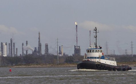 A tug boat navigates the Houston ship channel with a flare from an oil refinery and storage facility in the background south of downtown Hou A tug boat navigates the Houston ship channel with a flare from an oil refinery and storage facility in the background south of downtown Hou