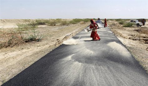 Women labourers throw dust on a road tarmac under construction at Bharadva village in the western Indian state of Gujarat April 23, 2013. RE Women labourers throw dust on a road tarmac under construction at Bharadva village in the western Indian state of Gujarat April 23, 2013. RE