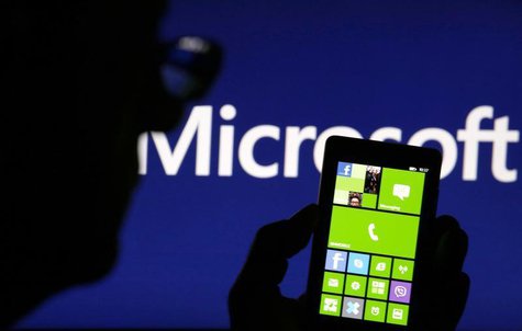 A man is silhouetted against a video screen with the Microsoft logo in the background as he poses with a Nokia Lumia 820 smartphone in this A man is silhouetted against a video screen with the Microsoft logo in the background as he poses with a Nokia Lumia 820 smartphone in this
