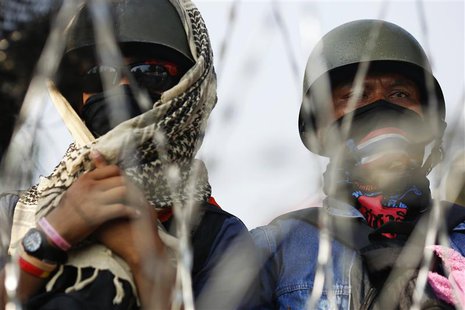 Masked anti-government protesters look out from behind a barricade near the Interior Ministry building, after a group of policemen who came Masked anti-government protesters look out from behind a barricade near the Interior Ministry building, after a group of policemen who came