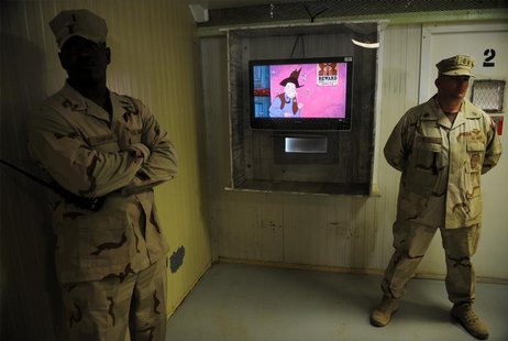 Guards stand next to a television showing a cartoon as journalists visit the movie room at the Camp Four detention facility at the U.S. Nava Guards stand next to a television showing a cartoon as journalists visit the movie room at the Camp Four detention facility at the U.S. Nava