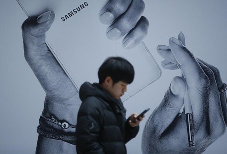 A passenger using his mobile phone walks past an advertisement promoting Samsung Electronics' Galaxy Note 3 at its exhibition hall at a rail A passenger using his mobile phone walks past an advertisement promoting Samsung Electronics' Galaxy Note 3 at its exhibition hall at a rail