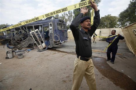 A security official uses a tape to cordon off a site of a damaged police bus after an explosion in Karachi February 13, 2014. REUTERS/Athar A security official uses a tape to cordon off a site of a damaged police bus after an explosion in Karachi February 13, 2014. REUTERS/Athar