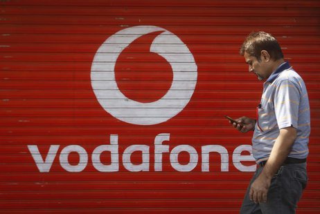 A man checks his mobile phone as he walks past a shop displaying the Vodafone logo on its shutter in Mumbai January 15, 2014. REUTERS/Danish A man checks his mobile phone as he walks past a shop displaying the Vodafone logo on its shutter in Mumbai January 15, 2014. REUTERS/Danish