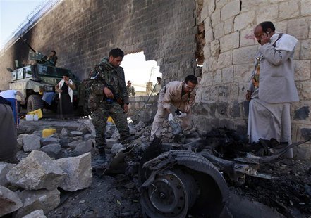 Investigators from the criminal investigation department (CID) examine the wreckage of a car after a bomb exploded outside the main wall of Investigators from the criminal investigation department (CID) examine the wreckage of a car after a bomb exploded outside the main wall of