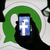 An illustration photo shows a man holding a smart phone with a Facebook logo as its screen wallpaper in front of a WhatsApp messenger logo, An illustration photo shows a man holding a smart phone with a Facebook logo as its screen wallpaper in front of a WhatsApp messenger logo,