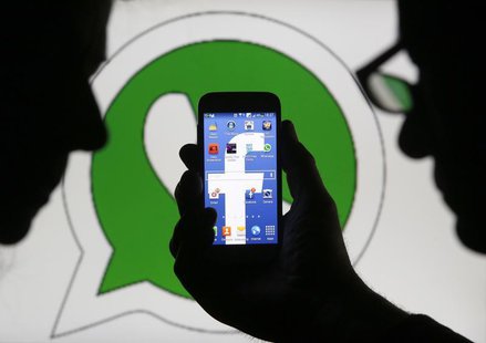 An illustration photo shows a man holding a smart phone with a Facebook logo as its screen wallpaper in front of a WhatsApp messenger logo, An illustration photo shows a man holding a smart phone with a Facebook logo as its screen wallpaper in front of a WhatsApp messenger logo,