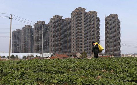 A farmer walks past a vegetable field near newly-built residential buildings in Jiaxing, Zhejiang province February 23, 2014. REUTERS/Willia A farmer walks past a vegetable field near newly-built residential buildings in Jiaxing, Zhejiang province February 23, 2014. REUTERS/Willia