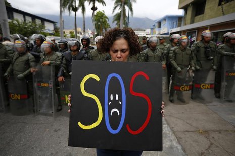 A demonstrator holds a placard as she stands in front of national guards during a protest near the Cuba's Embassy in Caracas February 25, 20 A demonstrator holds a placard as she stands in front of national guards during a protest near the Cuba's Embassy in Caracas February 25, 20