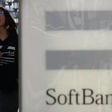A woman holding her smartphone walks past an advertisement board of SoftBank Corp outside its branch in Tokyo February 25, 2014. REUTERS/Yuy A woman holding her smartphone walks past an advertisement board of SoftBank Corp outside its branch in Tokyo February 25, 2014. REUTERS/Yuy