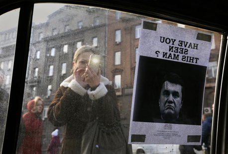 A woman takes photos of a "Wanted" notice for fugitive Ukrainian President Victor Yanukovich, plastered on the window of a car used as a bar A woman takes photos of a "Wanted" notice for fugitive Ukrainian President Victor Yanukovich, plastered on the window of a car used as a bar