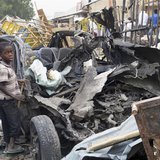 Two boys stand near the charred chassis of a vehicle after a bomb attack near a busy market area in Ajilari-Gomari near the city's airport, Two boys stand near the charred chassis of a vehicle after a bomb attack near a busy market area in Ajilari-Gomari near the city's airport,