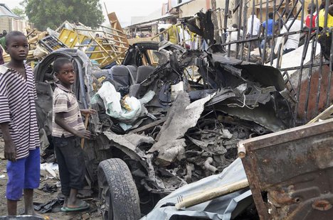 Two boys stand near the charred chassis of a vehicle after a bomb attack near a busy market area in Ajilari-Gomari near the city's airport, Two boys stand near the charred chassis of a vehicle after a bomb attack near a busy market area in Ajilari-Gomari near the city's airport,
