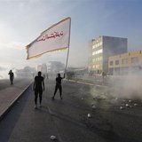 An anti-government protester waves a flag with a religious slogan on it as he confronts riot police amidst teargas, during clashes after the An anti-government protester waves a flag with a religious slogan on it as he confronts riot police amidst teargas, during clashes after the