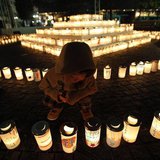 A boy looks at a candle light with a character reading: "bond", written on the candle holder at a memorial held in remembrance of victims of A boy looks at a candle light with a character reading: "bond", written on the candle holder at a memorial held in remembrance of victims of