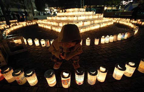 A boy looks at a candle light with a character reading: "bond", written on the candle holder at a memorial held in remembrance of victims of A boy looks at a candle light with a character reading: "bond", written on the candle holder at a memorial held in remembrance of victims of