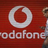 A man checks his mobile phone as he walks past a shop displaying the Vodafone logo on its shutter in Mumbai January 15, 2014. REUTERS/Danish A man checks his mobile phone as he walks past a shop displaying the Vodafone logo on its shutter in Mumbai January 15, 2014. REUTERS/Danish