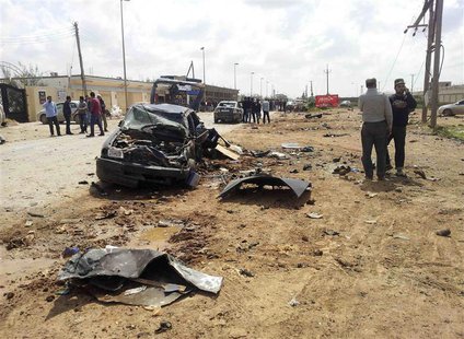 Men stand next to a car damaged after an explosion exploded outside a Libyan army base in the eastern city of Benghazi March 17, 2014. REUTE Men stand next to a car damaged after an explosion exploded outside a Libyan army base in the eastern city of Benghazi March 17, 2014. REUTE