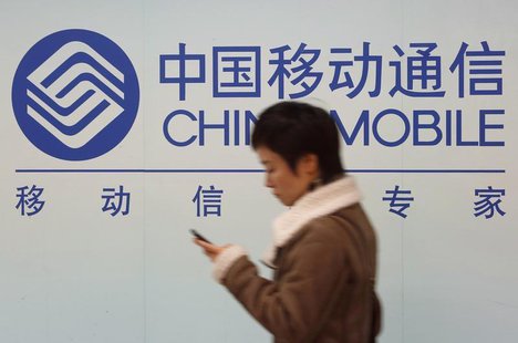 A woman looks at the screen of her mobile phone while walking past a China Mobile sign in downtown Shanghai December 18, 2013 file photo. RE A woman looks at the screen of her mobile phone while walking past a China Mobile sign in downtown Shanghai December 18, 2013 file photo. RE