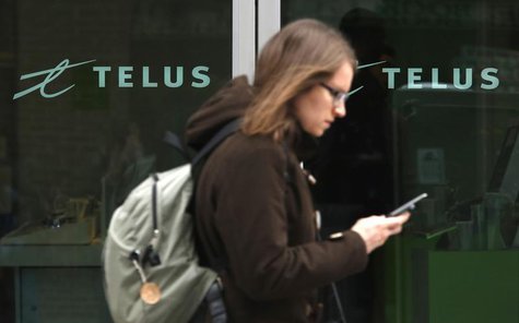 A woman uses a mobile device while walking past a Telus store in Ottawa February 19, 2014. REUTERS/Chris Wattie A woman uses a mobile device while walking past a Telus store in Ottawa February 19, 2014. REUTERS/Chris Wattie