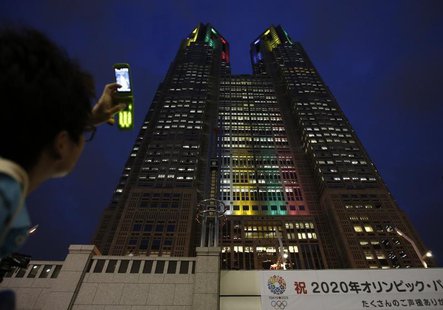A visitor takes photos of Tokyo Metropolitan Government Building illuminated in the Olympic colors before an event titled "Tokyo 2020 Host C A visitor takes photos of Tokyo Metropolitan Government Building illuminated in the Olympic colors before an event titled "Tokyo 2020 Host C
