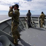 Gunner Richard Brown (L) of Transit Security Element looks through binoculars as he stands on lookout with other crew members aboard the Aus Gunner Richard Brown (L) of Transit Security Element looks through binoculars as he stands on lookout with other crew members aboard the Aus
