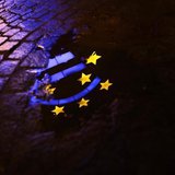 The Euro sculpture is partially reflected in a puddle on a cobblestone pavement in front of the headquarters of the European Central Bank (E The Euro sculpture is partially reflected in a puddle on a cobblestone pavement in front of the headquarters of the European Central Bank (E