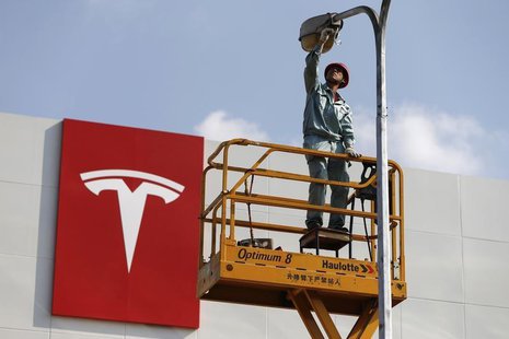 A labourer repairs a street lamp next to a logo of Tesla Motors in front of a new showroom of the company in Shanghai, April 22, 2014. REUTE A labourer repairs a street lamp next to a logo of Tesla Motors in front of a new showroom of the company in Shanghai, April 22, 2014. REUTE