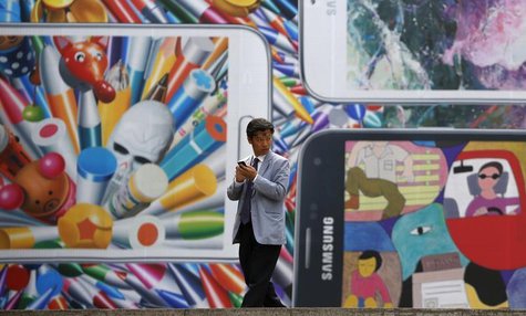 A man uses his mobile phone in front of a giant advertisement promoting Samsung Electronics' new Galaxy S5 smartphone, at an art hall in cen A man uses his mobile phone in front of a giant advertisement promoting Samsung Electronics' new Galaxy S5 smartphone, at an art hall in cen
