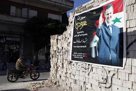 A man on a motorcycle rides past a poster depicting Syria's President Bashar al-Assad on a wall in the pro-government al-Zahraa neighbourhoo A man on a motorcycle rides past a poster depicting Syria's President Bashar al-Assad on a wall in the pro-government al-Zahraa neighbourhoo